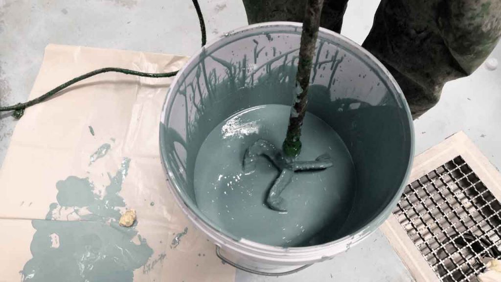 Grey epoxy resin being mixed in a bucket with a paddle mixer before application