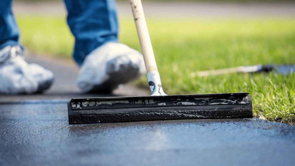 Applying dark protective sealant coating along a driveway edge with a squeegee
