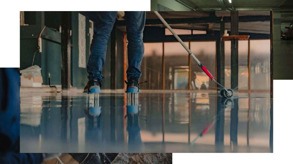 Installer in spiked shoes spreading wet epoxy across a glossy garage floor