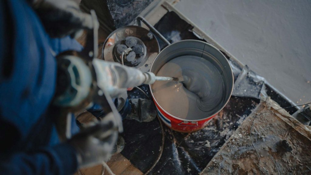 Tradesman using a mixing drill to blend epoxy resin before pouring it onto a floor