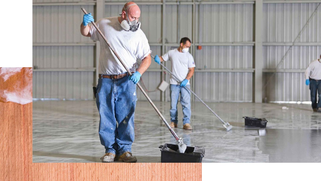 Two tradesmen applying grey epoxy coating across a large garage floor using rollers and squeegees