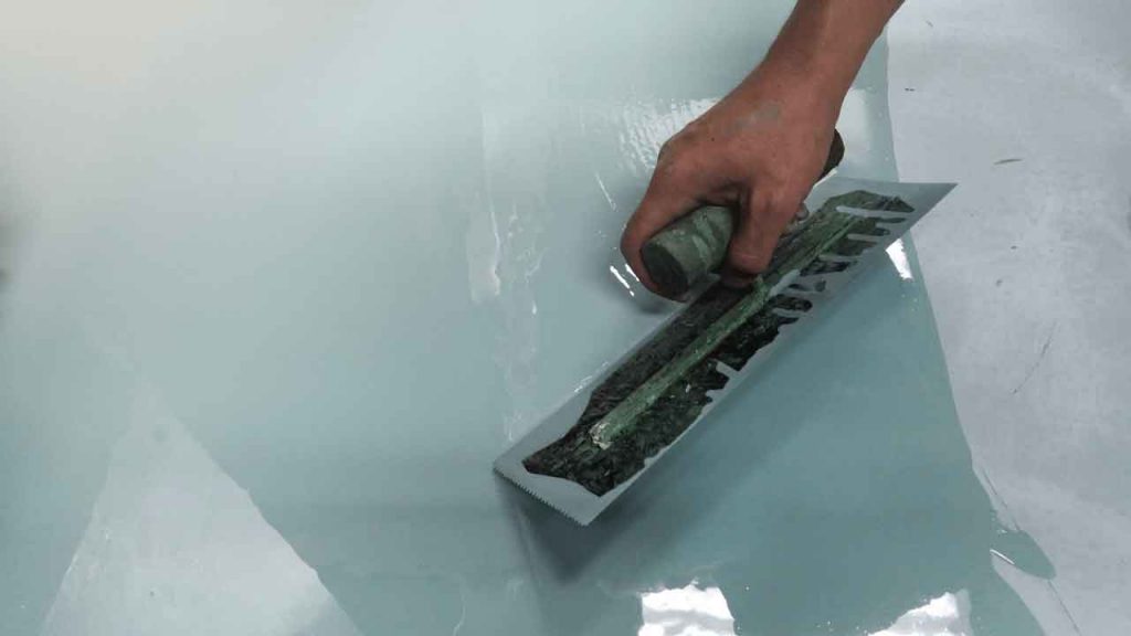 Close-up of a hand smoothing pale blue-grey epoxy coating with a trowel