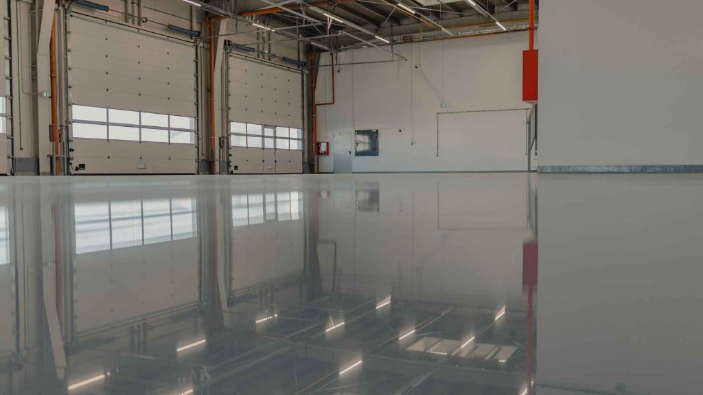 Finished glossy grey epoxy floor inside a warehouse with roller doors and reflected lighting