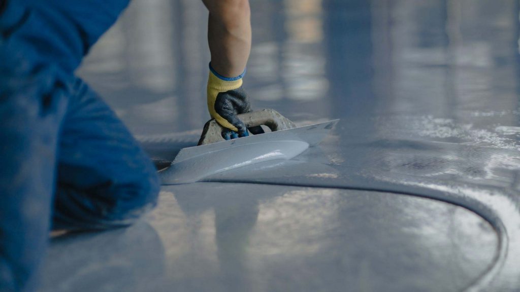 Close-up of a trowel smoothing fresh grey epoxy resin flooring