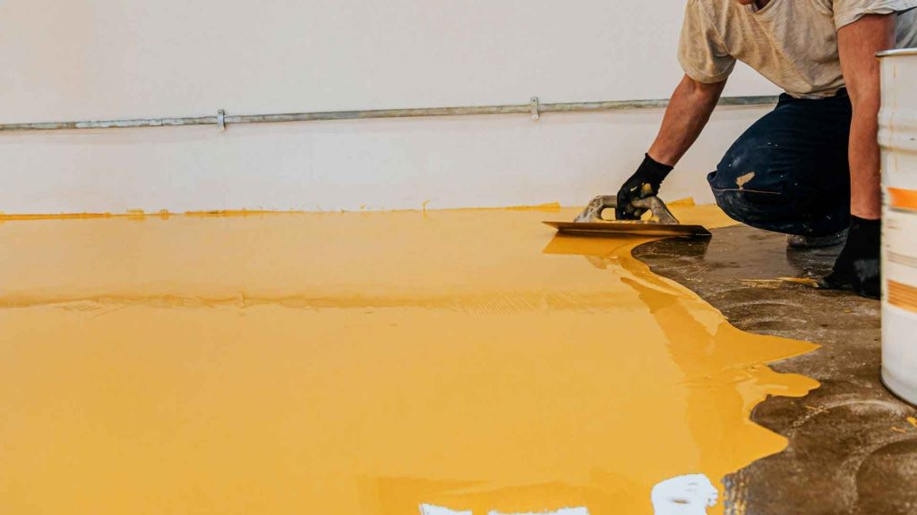 Tradesman trowelling a golden yellow epoxy coating onto a warehouse floor
