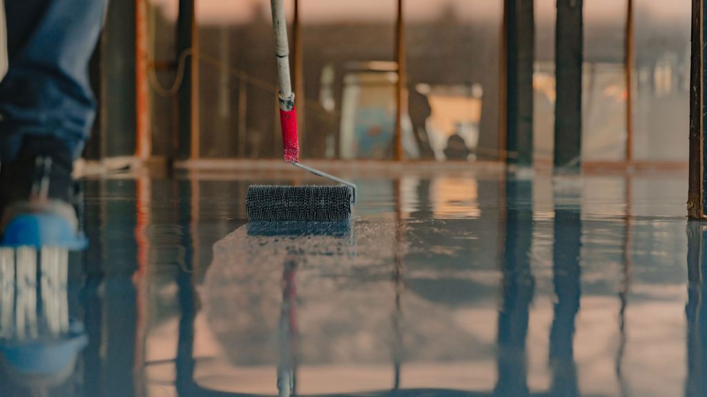 Worker using a roller to apply a glossy floor coating during an epoxy flooring installation