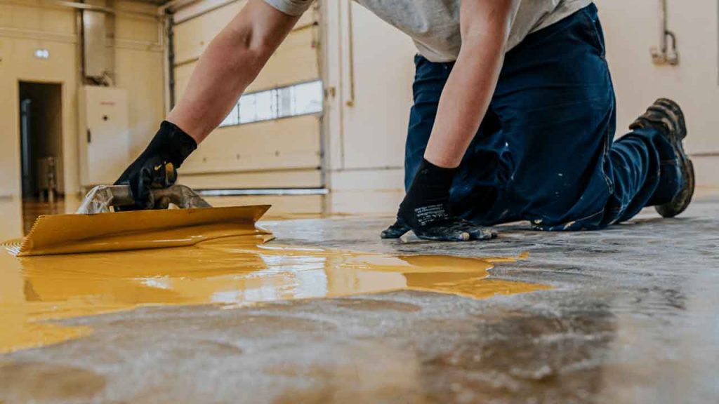 Tradesman troweling a yellow epoxy resin coat onto a garage floor