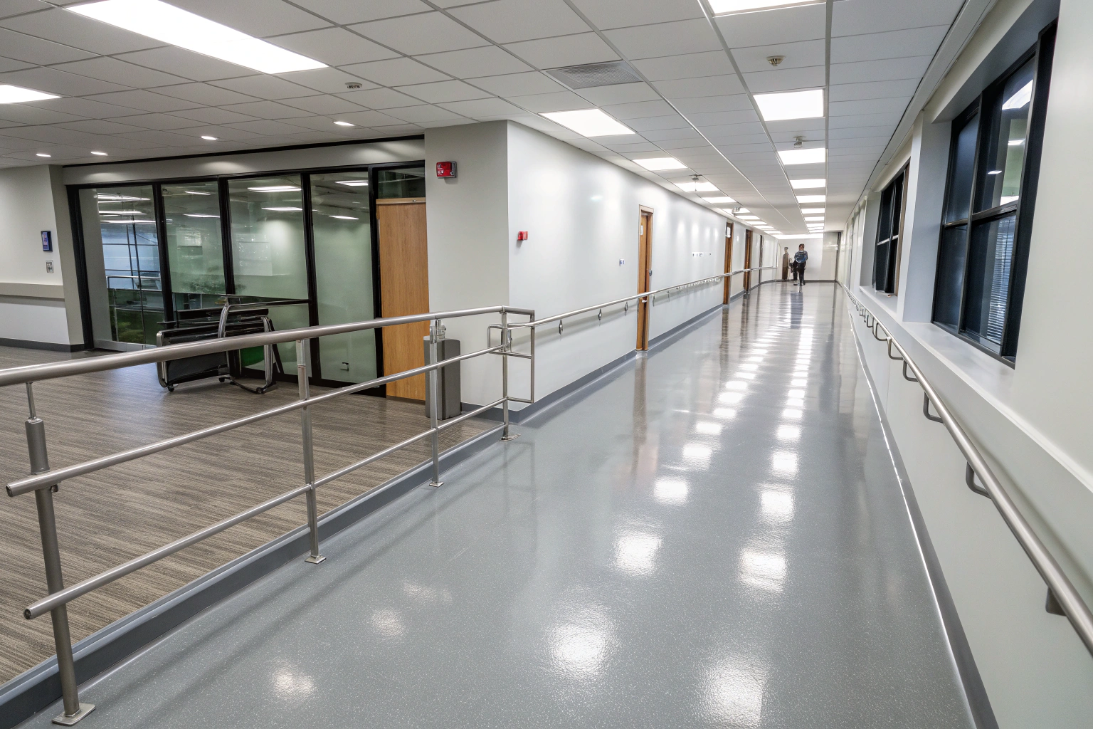 Glossy grey epoxy corridor floor in a Newcastle facility with handrails and glass office walls