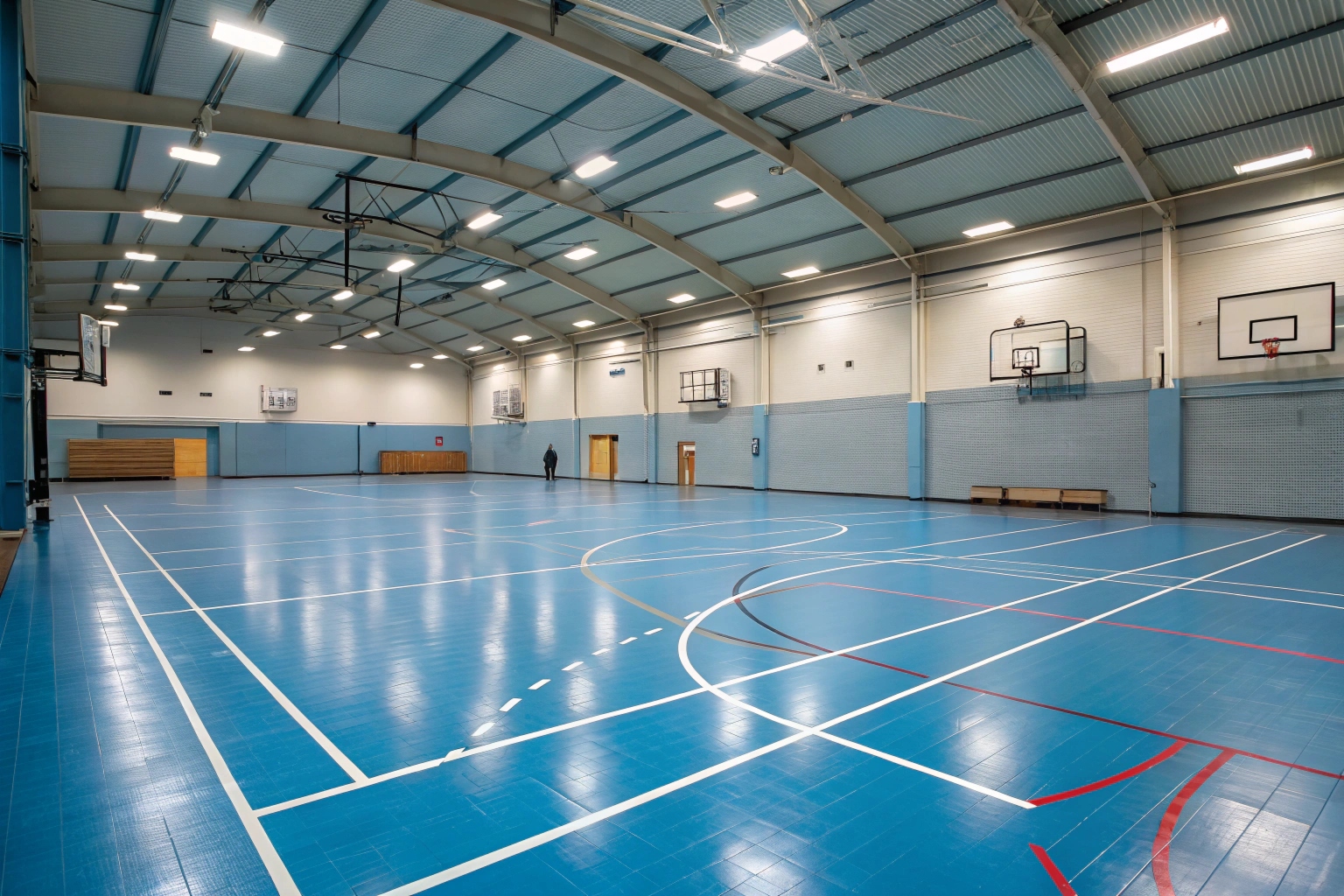 Indoor school sports hall with blue epoxy floor coating, court markings, and basketball hoops